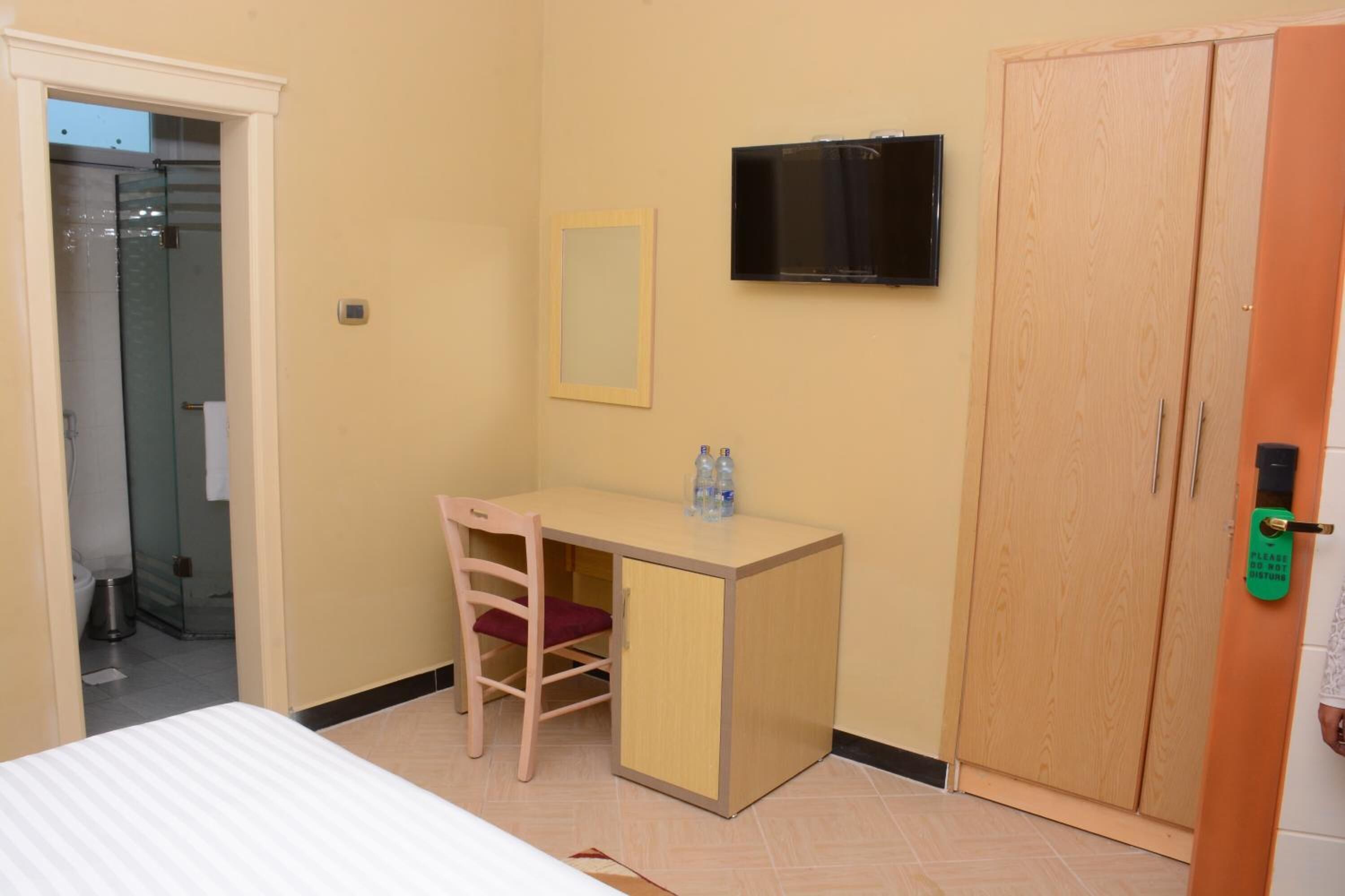 A room with a bed, a desk with a chair, a television mounted on the wall, and a wardrobe.