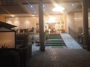 Un vestíbulo de hotel con mostrador de recepción, una escalera y una zona de estar con plantas en macetas.
