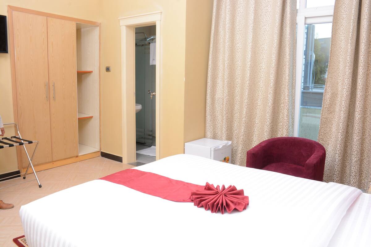 A hotel room with a bed, a wardrobe, a bathroom, and a window with curtains.