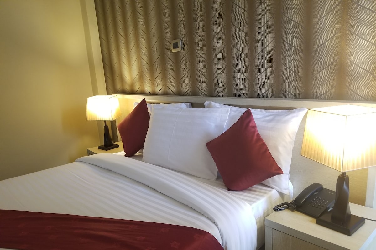 A hotel room with a neatly made bed, two bedside lamps, a telephone, and a small drawer.