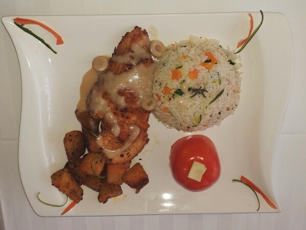 Un plato con pollo a la parrilla, arroz y tomate.