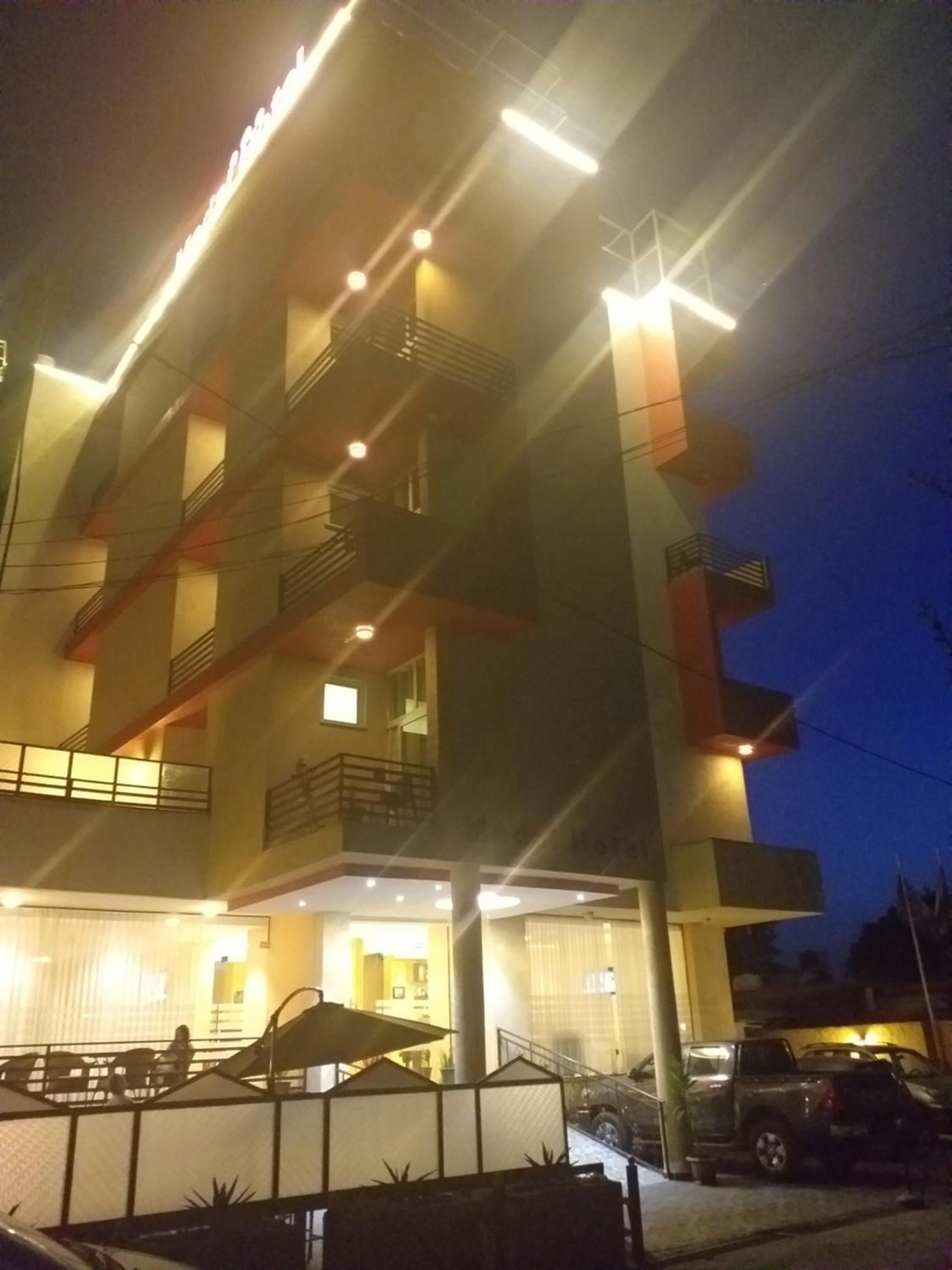 Un hotel de varios pisos con balcones, una zona de estar al aire libre cubierta y un estacionamiento.
