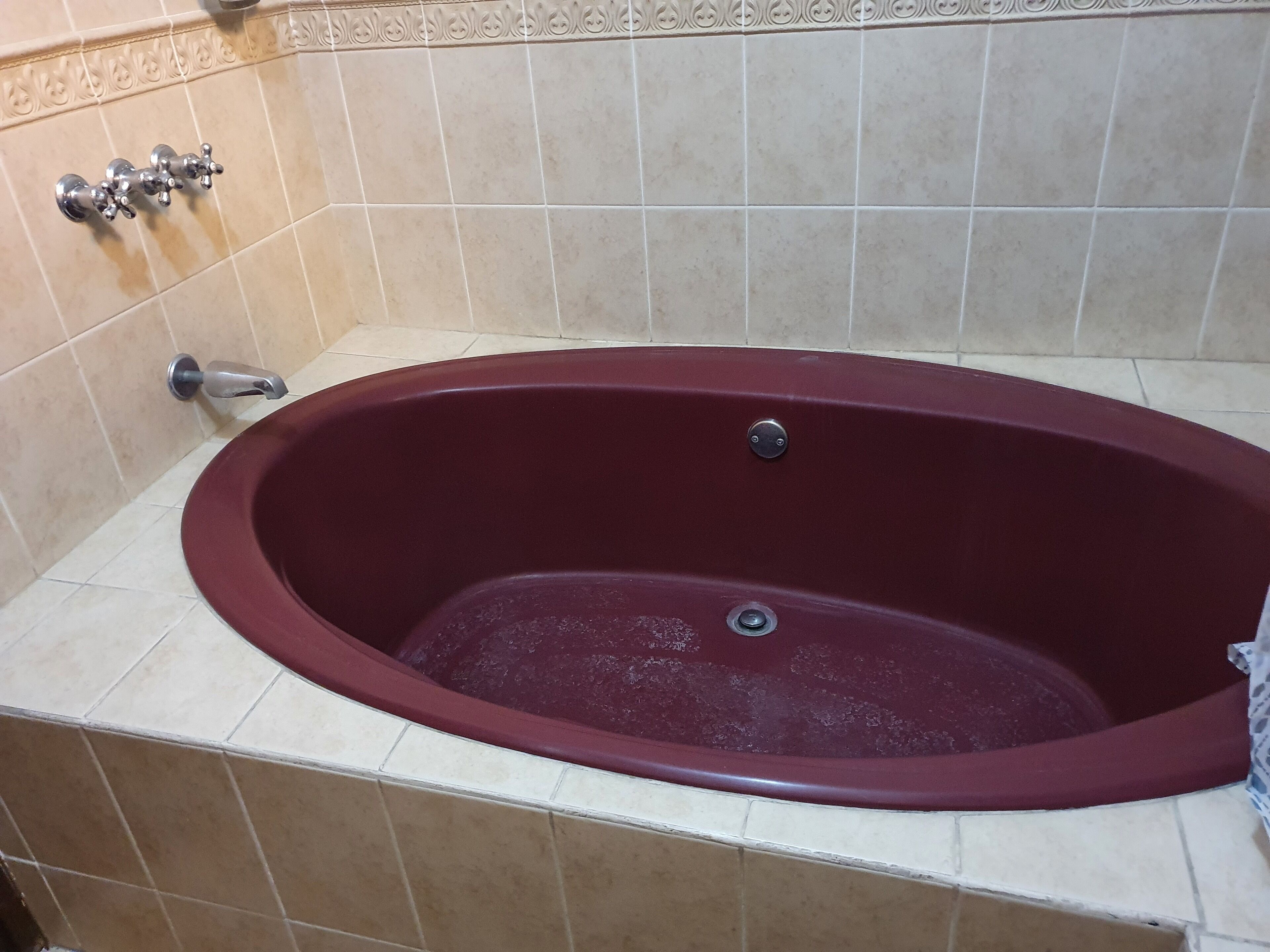 A bathtub with a red interior, a faucet, and a drain.