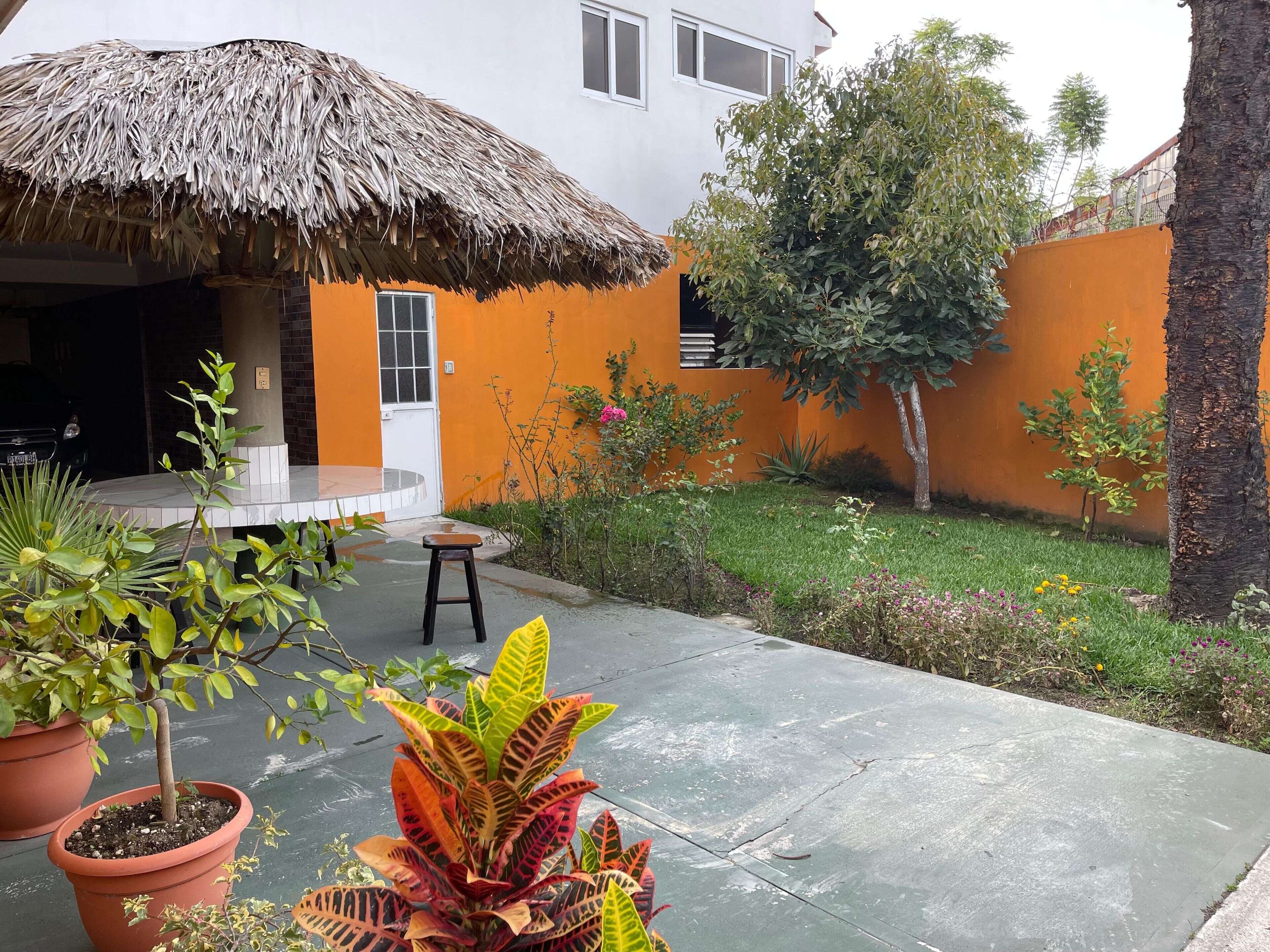 A courtyard with a thatched roof, potted plants, and a small table.