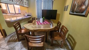 A dining area with a round wooden table, six wooden chairs, a TV on the wall, and a window with patterned curtains. - Casa hermosa a 20 minutos del aeropuerto (Guatemala City)