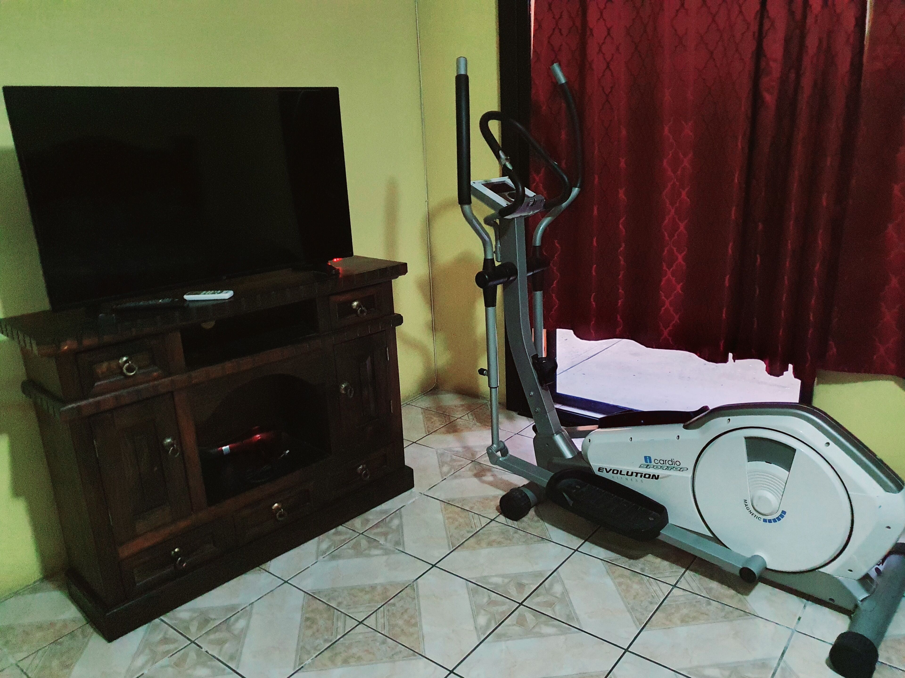 Una habitación con un armario de madera, un televisor y una bicicleta estática.