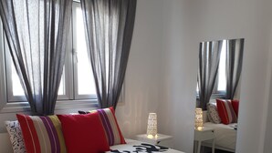 A neatly arranged bedroom with a large bed, a bedside table with a lamp, and a window with curtains. - Eva Christ Apt (Oroklini)