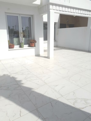 A spacious outdoor area with white tiled flooring and potted plants near the windows. - Eva Christ Apt (Oroklini)