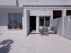Ein modernes Gebäude mit weißer Fassade, einer gefliesten Terrasse und einer kleinen Sitzecke mit zwei Stühlen.