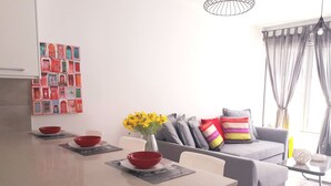 A modern kitchen with a dining area, a grey sofa with colorful cushions, and a vase with yellow flowers. - Eva Christ Apt (Oroklini)