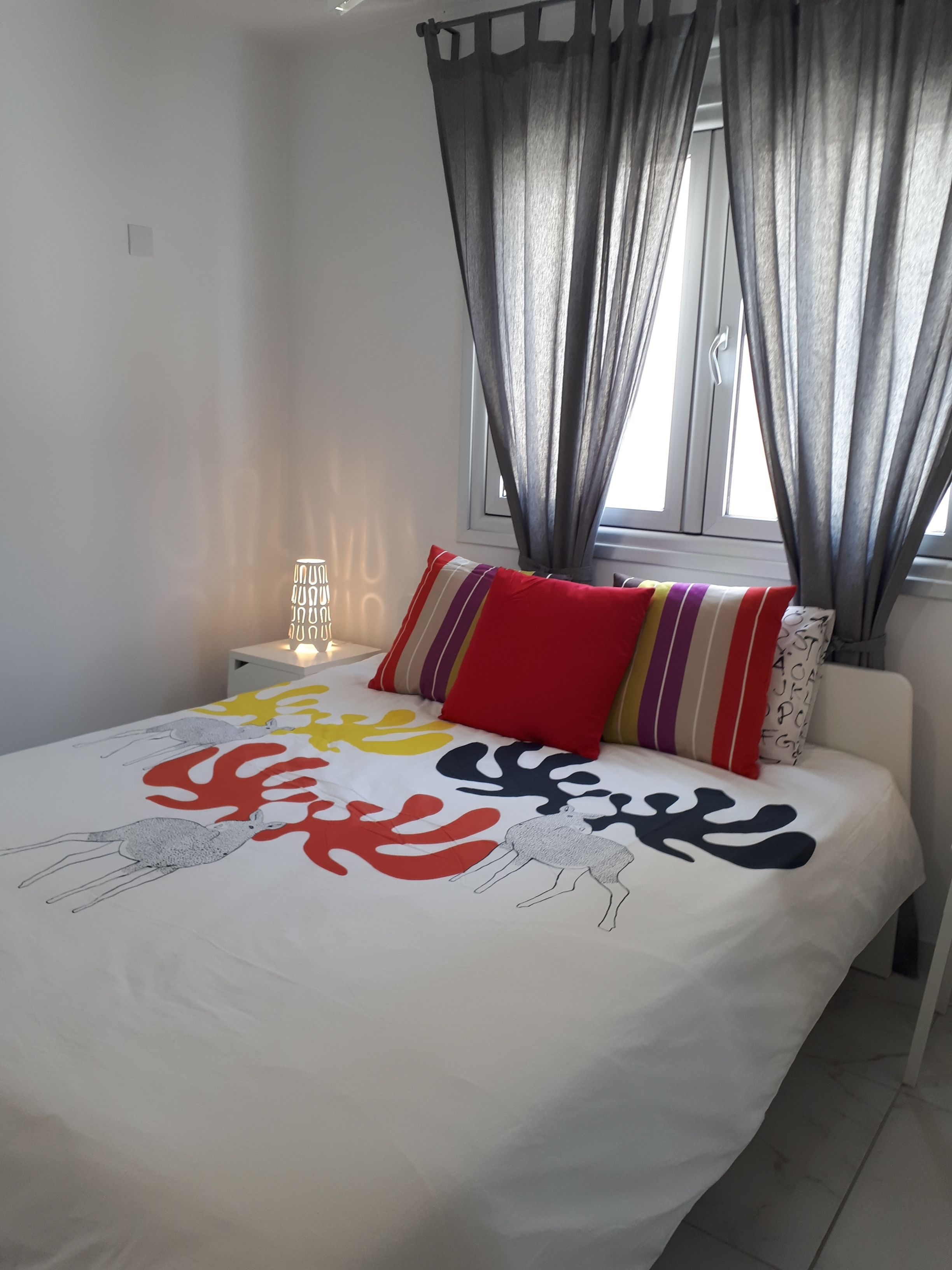 A bed with a colorful bedspread, a bedside lamp, and a window with curtains.