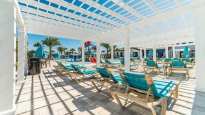 A covered pool area with sun loungers and a water slide.