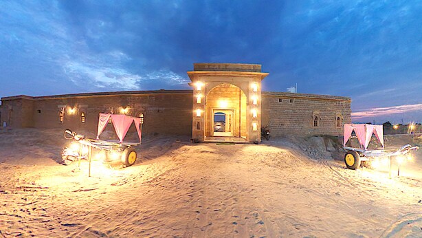 A building with a central entrance, flanked by two carts with pink canopies, under a twilight sky.