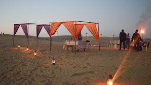 A desert campsite with tents, a table set for dining, and lanterns providing light.