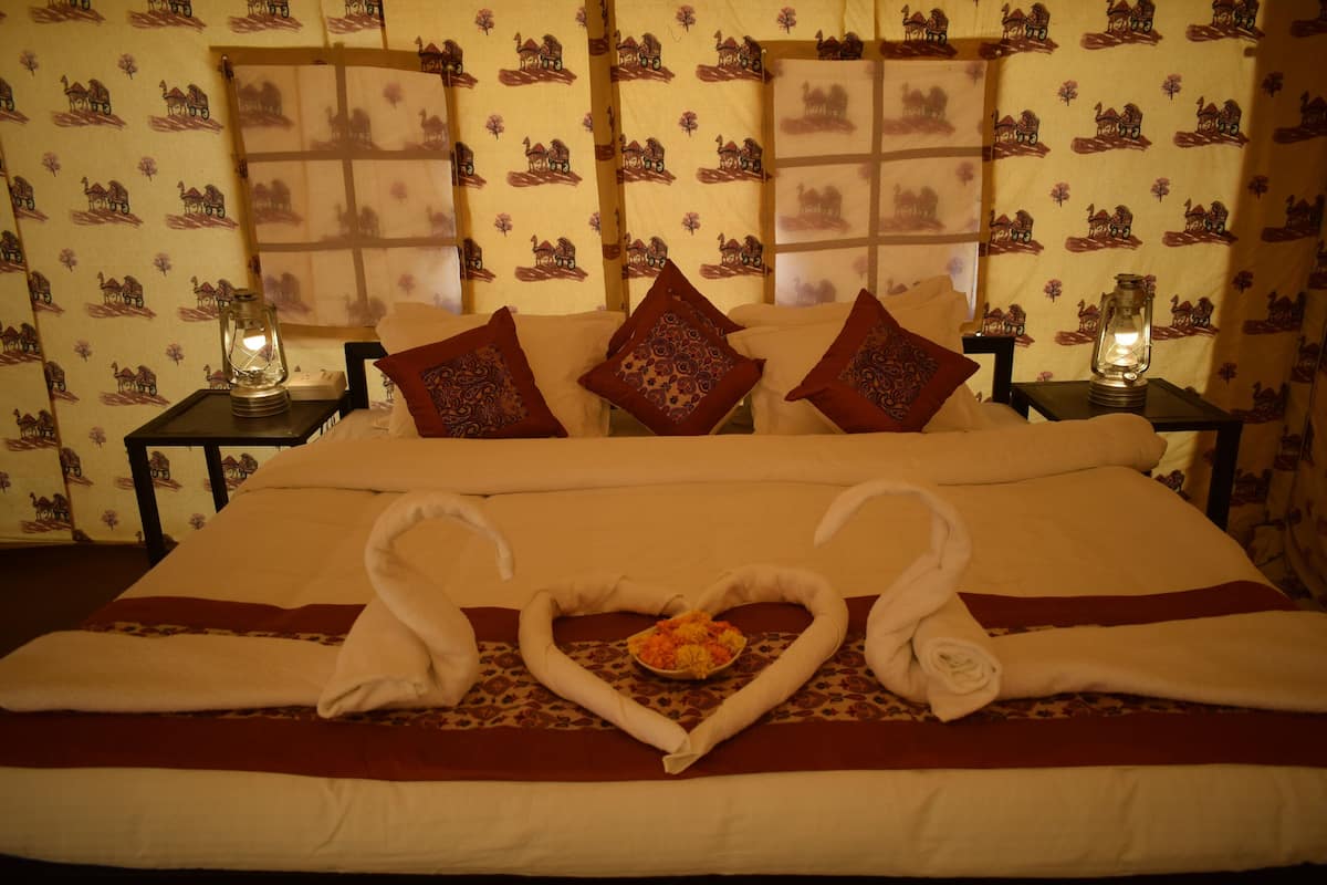 Un lit agrémenté d’une décoration en forme de cœur réalisée avec des serviettes, de deux cygnes, d’un panier de fruits et d’oreillers à motifs.
