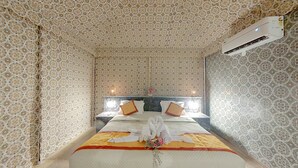 A hotel room with a patterned wallpaper, a bed with towels, a nightstand, and an air conditioning unit.