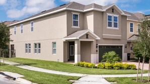 A two-story residential building with a beige exterior, a front porch, and a garage. - The Encore Club #7 - 8 Bed 7 Baths Villa (Kissimmee)