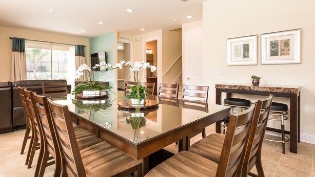 A dining area with a glass-top table, wooden chairs, and potted plants. - The Encore Club #7 - 8 Bed 7 Baths Villa (Kissimmee)