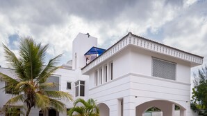 A white building with a balcony, palm trees, and a paved entrance. - Nyali Villa (Mombasa)
