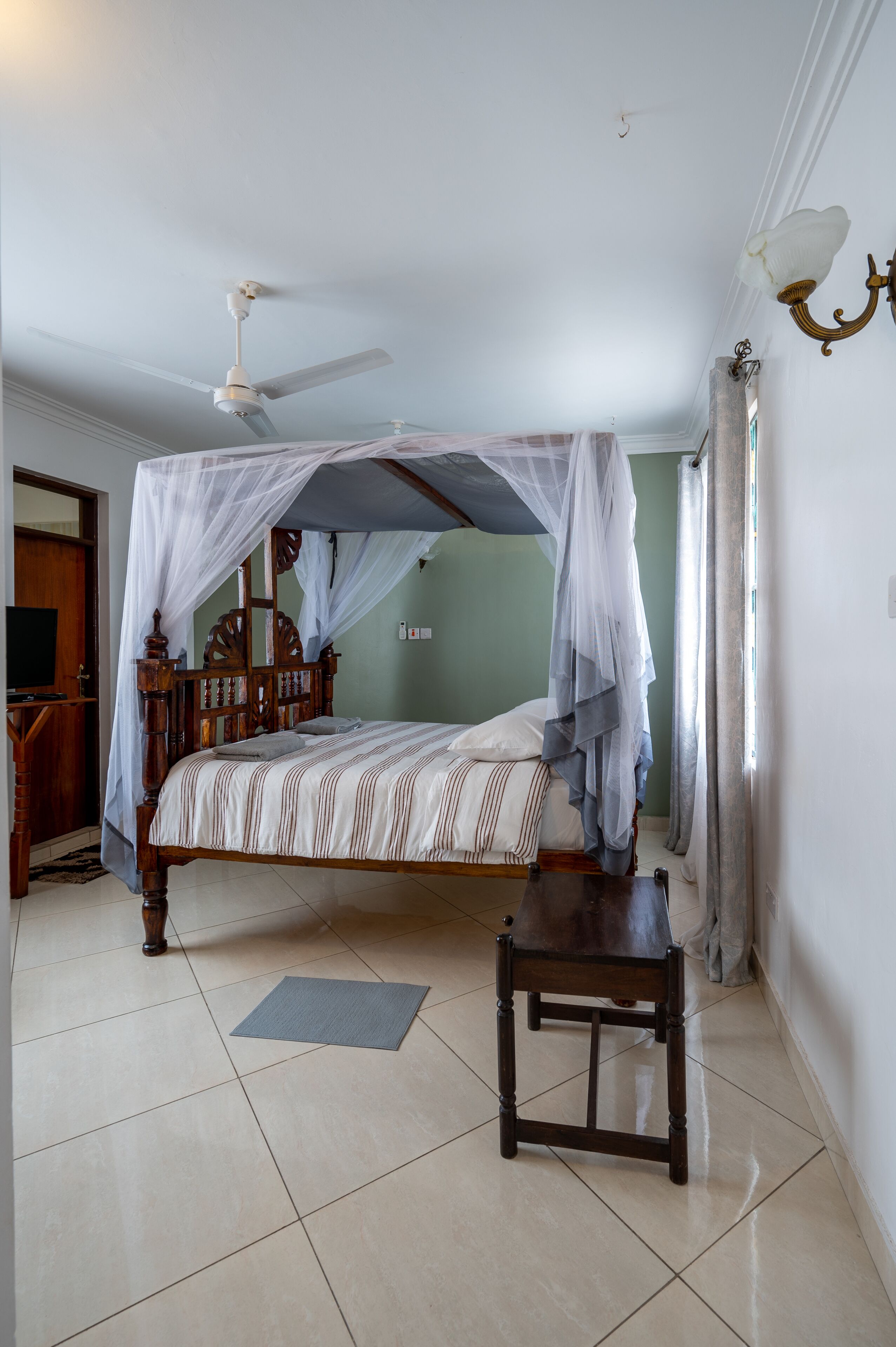 Een slaapkamer met een hemelbed, een plafondventilator en een nachtkastje.