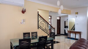 A dining area with a glass table and black chairs, a staircase with a metal railing, and a living room with a brown leather sofa. - Nyali Villa (Mombasa)