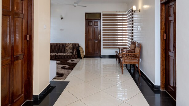 A hallway with a tiled floor, wooden doors, a ceiling fan, and a seating area with a patterned sofa and chairs. - Nyali Villa (Mombasa)