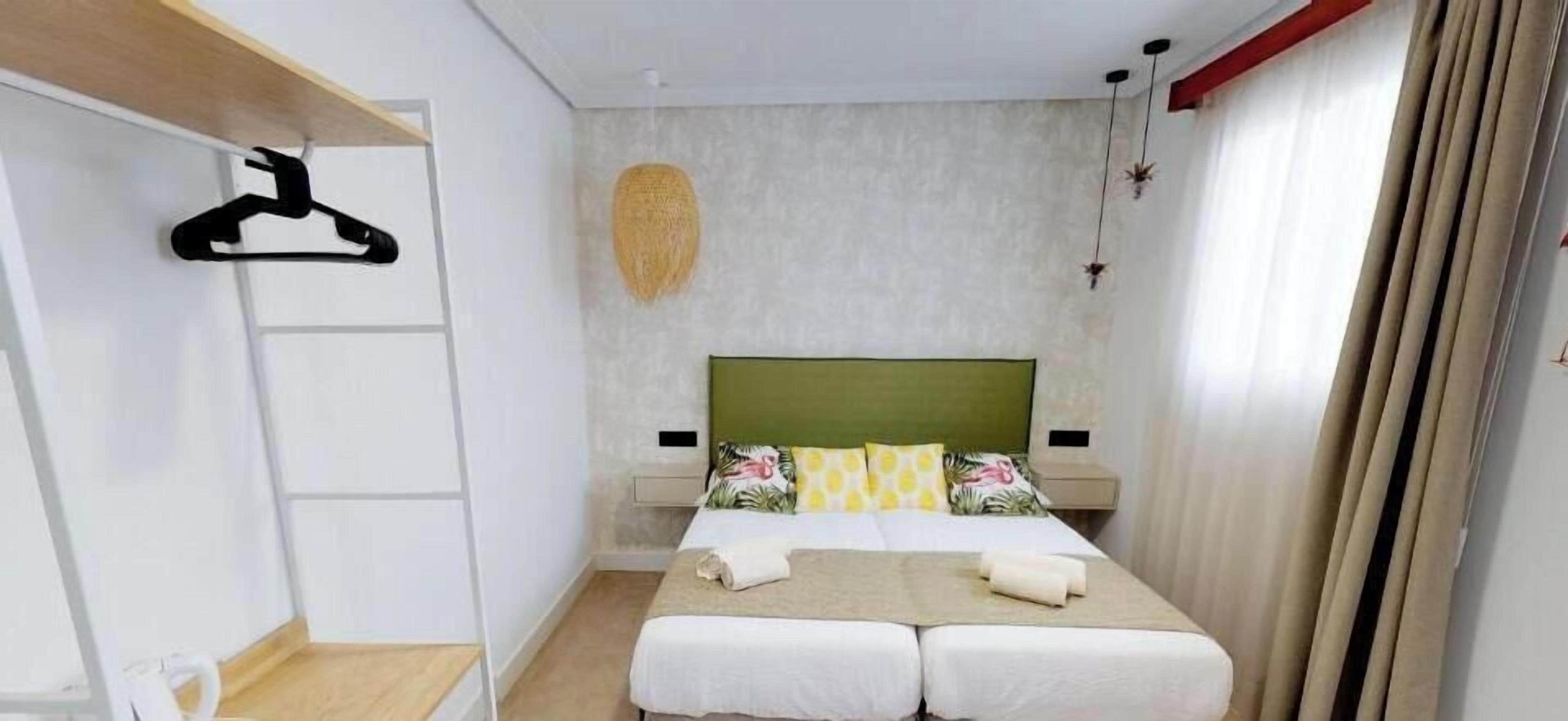 A hotel room with a bed, a hanging plant, a wardrobe, and a window with curtains.