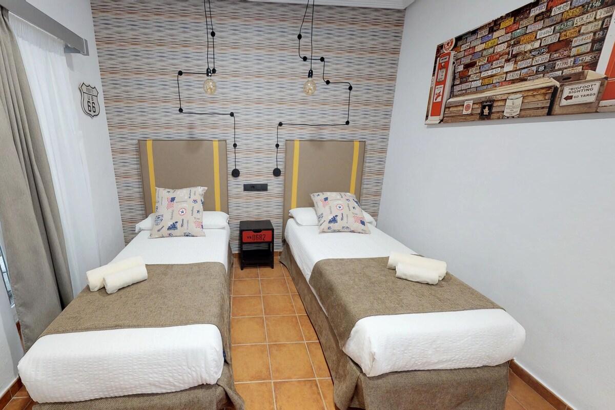 A hotel room with two beds, a small table, and a wall with a Route 66 sign.
