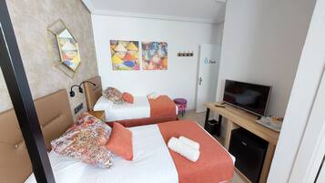 Habitación de hotel con dos camas, televisión, escritorio con computadora y un refrigerador pequeño.