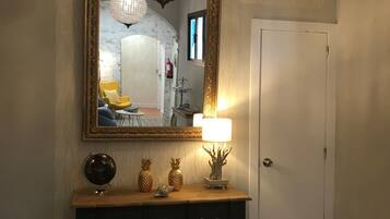 A hallway with a large ornate mirror, a chandelier, a wooden console table with decorative items, and a white door.