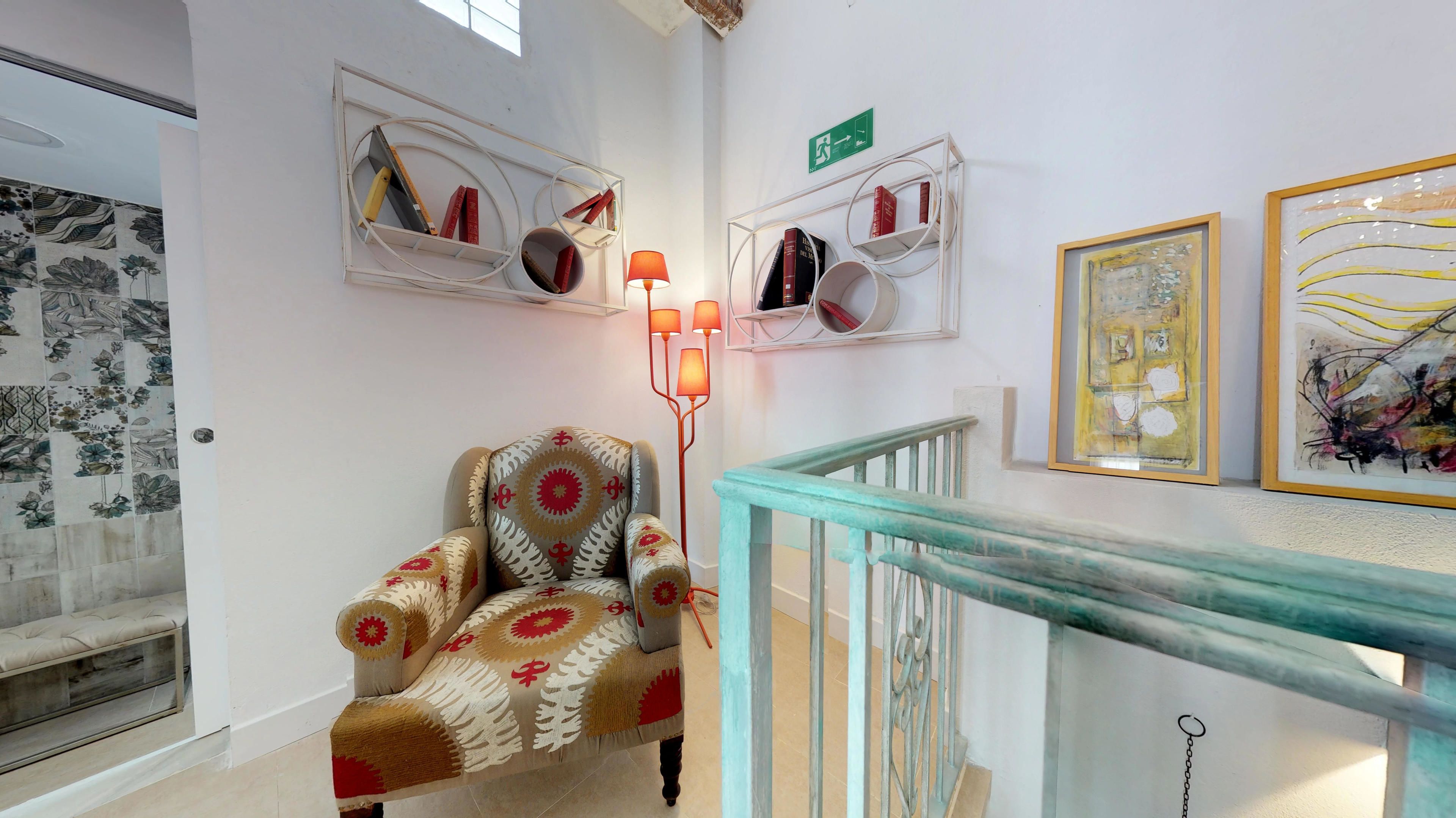 Una habitación con un sillón estampado, una escalera con barandilla verde aguamarina y obras de arte en las paredes.