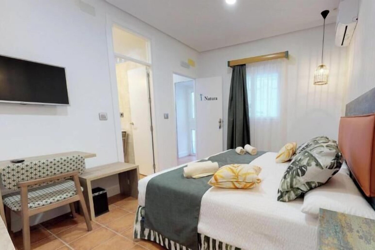 A hotel room with a bed, a desk, a chair, a TV, and a door.
