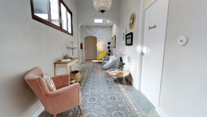 Un pasillo con piso estampado, una silla rosa, un sillón amarillo, una mesa redonda con libros y una puerta que indica “Privado”.