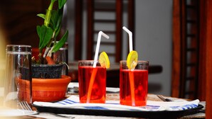 Three glasses of red beverage with straws and lemon slices, a potted plant, and a tray with a napkin and utensils. - Sun Ceylon Habarana (Sigiriya)