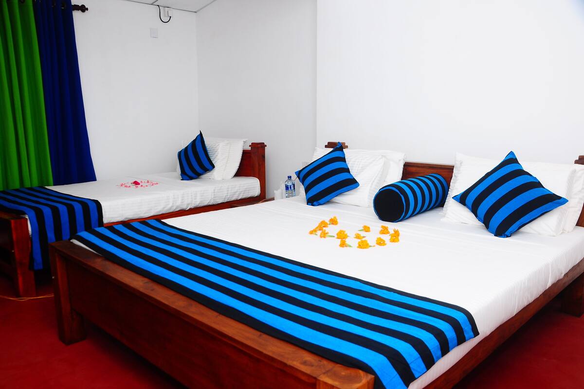 A hotel room with two single beds, each with blue and white bedding, and a large bed with blue and white bedding.