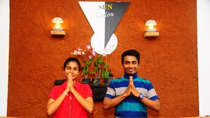 Two people standing in front of a wall with a logo and two wall-mounted lights. - Sun Ceylon Habarana (Sigiriya)