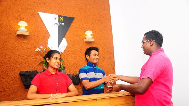 A reception desk with a sign reading "SUN Ceylon" and two wall-mounted light fixtures. - Sun Ceylon Habarana (Sigiriya)