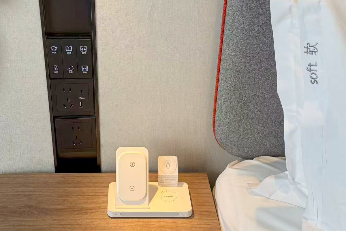 Et hotelværelse med et sengebord, en strømfordeler og en opladestation.