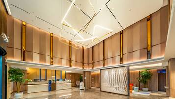 A spacious lobby with a reception desk, modern lighting fixtures, and a large plant.