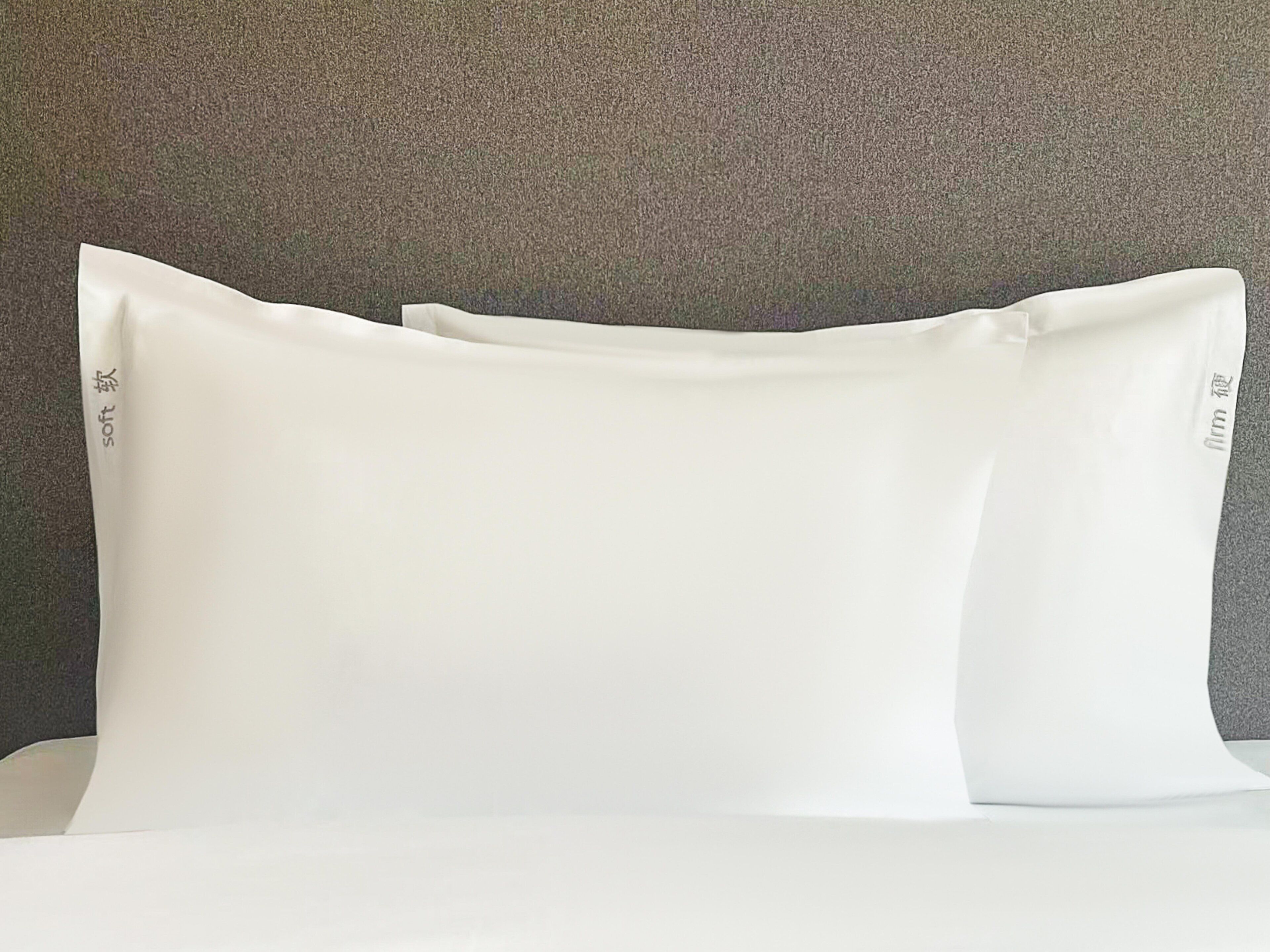 A bed with white pillows and a grey textured wall in the background.