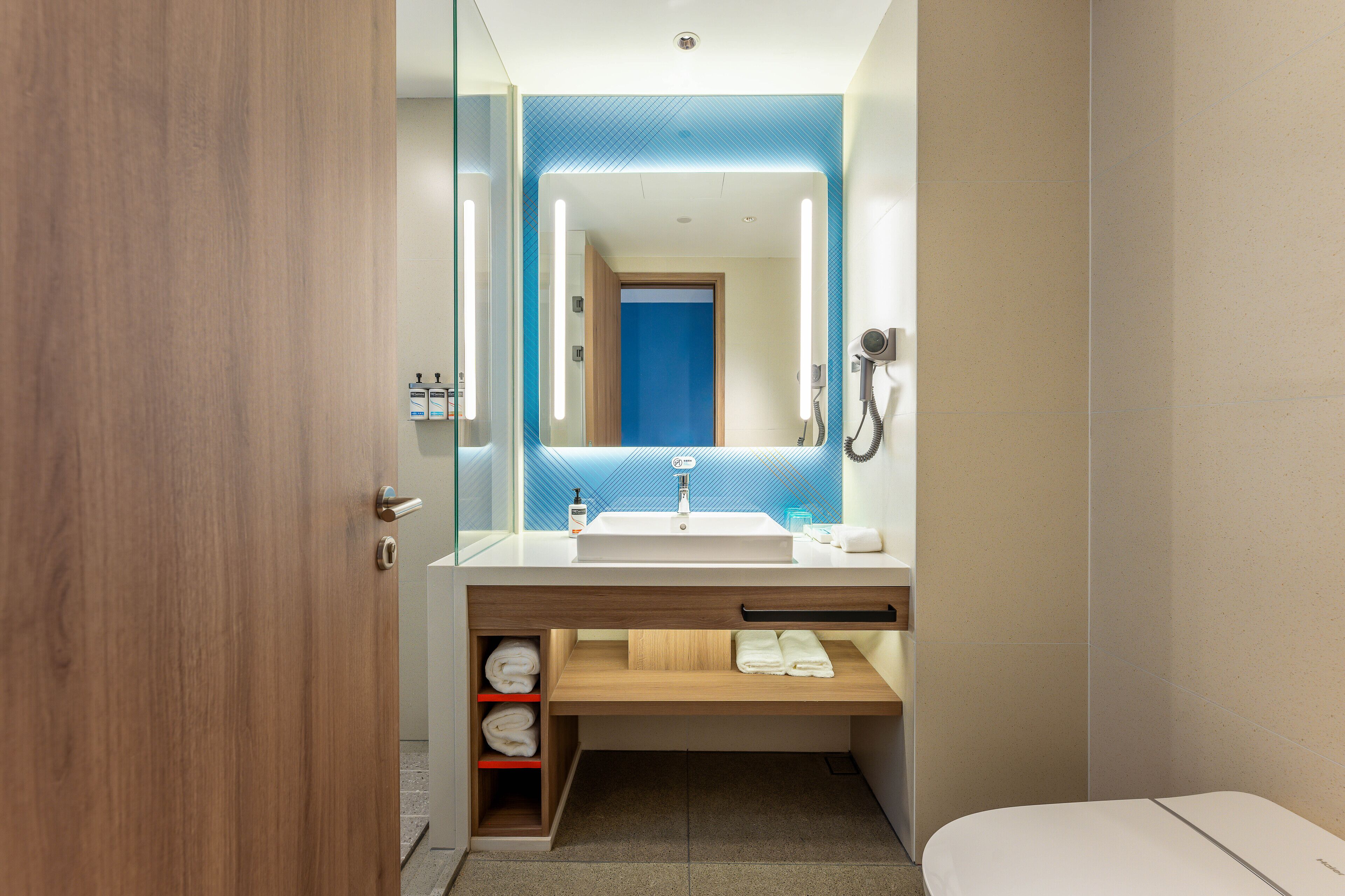 Un baño moderno con tocador de madera, un espejo grande y un estante empotrado con toallas.