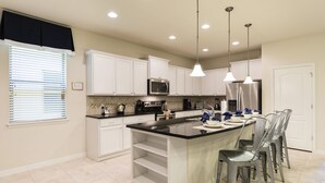 A modern kitchen with white cabinets, a black countertop, and stainless steel appliances. There are pendant lights, a window with blinds, and a door. - Windsor at Westside #20 - 9 Bedroom Private Pool Villa in Brand New Resort (Kissimmee)