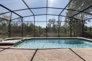 A swimming pool with a clear view of the surrounding trees and a covered area with a brick floor.