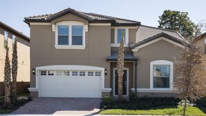 A two-story house with a white garage door, a small front porch, and a tree in the front yard. - Windsor at Westside #20 - 9 Bedroom Private Pool Villa in Brand New Resort (Kissimmee)