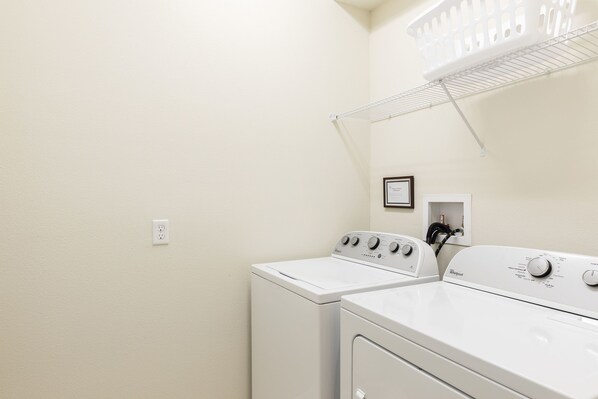 A laundry room with two white Whirlpool washers, a white shelf with a picture, and a white ceiling fan.