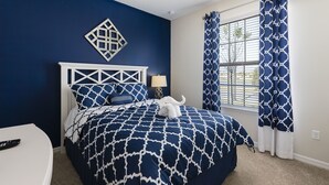 A bedroom with a bed, a nightstand, a lamp, and a decorative wall piece. - Windsor at Westside #20 - 9 Bedroom Private Pool Villa in Brand New Resort (Kissimmee)