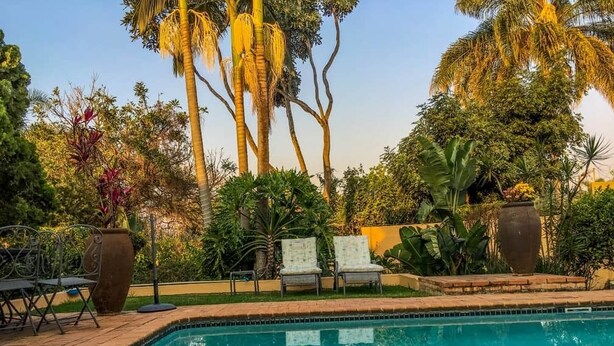 Una piscina con sillas de descanso y un área de terraza con baldosas, rodeada de diversas plantas y árboles tropicales.