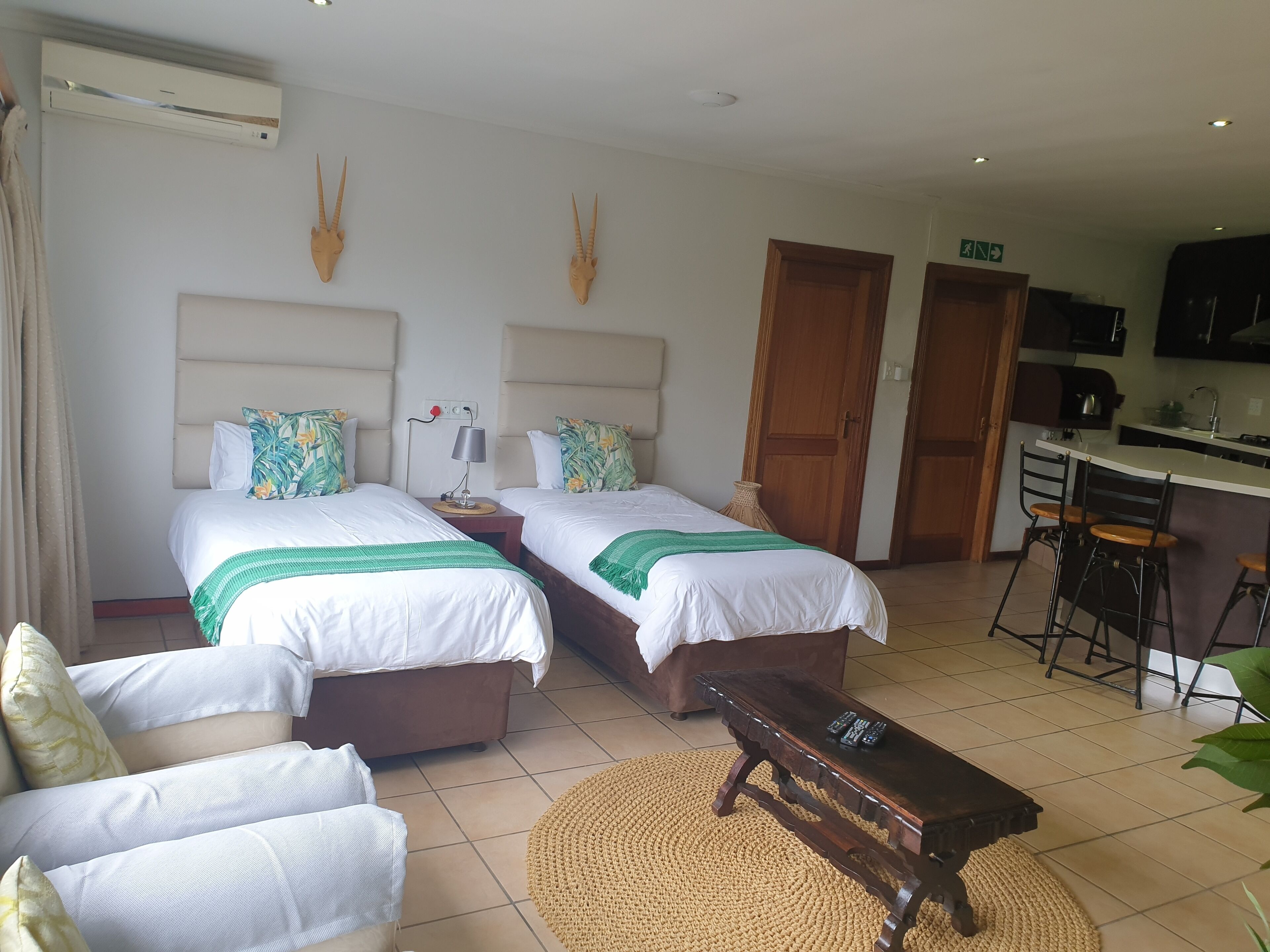 Habitación de hotel con dos camas, un escritorio pequeño, una silla, un banco y una kitchenette.