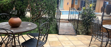 An outdoor patio area with a round table and chairs, a pathway leading to a pool, and a building in the background.