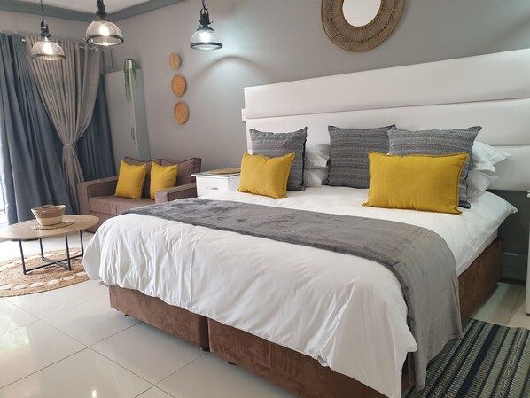 A modern bedroom with a large bed, bedside tables, a small round table, and a decorative wall piece.